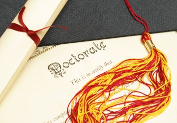 A closeup shot of a doctorate and diploma scroll with the tassels of a mortar board.